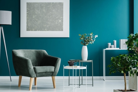 A modern chair sits with nesting side tables in front of a teal wall