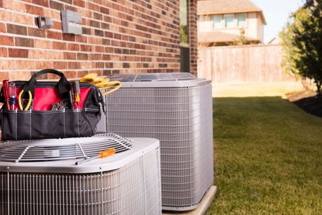 A tool bag sits on top of an air conditioning unit in a backyard