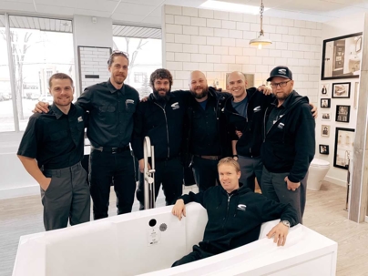 A team of professional plumbers gather around a bathtub