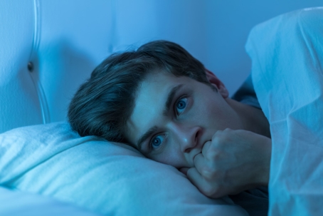 A person lays awake in bed with a nervous expression